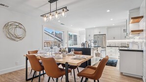 Una cocina moderna con armarios blancos, un refrigerador de acero inoxidable y un comedor con mesa de madera y sillas marrones.