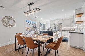 Eine moderne Küche mit weißen Schränken, einem Edelstahlkühlschrank und einem Essbereich mit einem Holztisch und braunen Stühlen.