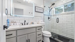 Un baño moderno con tocador blanco, un espejo grande y zona de ducha.