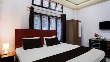 A hotel room with a bed, a desk, a TV, and a window with curtains.