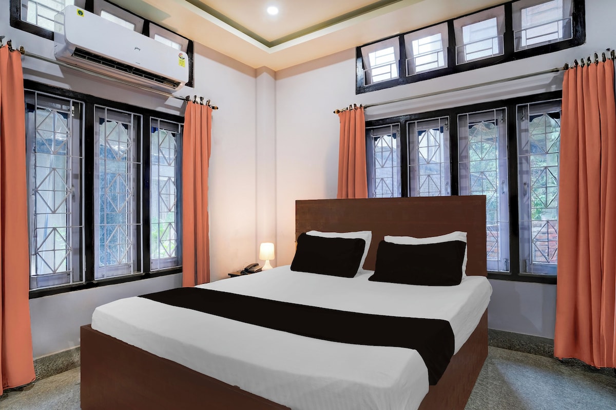 Une chambre d’hôtel avec un grand lit, deux fenêtres avec des rideaux, un appareil de climatisation et une table de chevet avec une lampe.