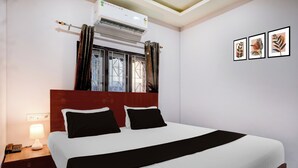 A hotel room with a bed, a nightstand, a lamp, an air conditioner, a window with curtains, and wall art. - Collection O Guwahati Airport (Guwahati)