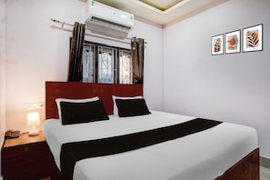 Une chambre d’hôtel comprenant un lit, une table de chevet, une lampe, un climatiseur, une fenêtre avec des rideaux et des œuvres d’art murales.