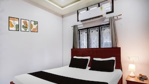 A hotel room with a bed, a nightstand, a lamp, and an air conditioning unit. - Collection O Guwahati Airport (Guwahati)