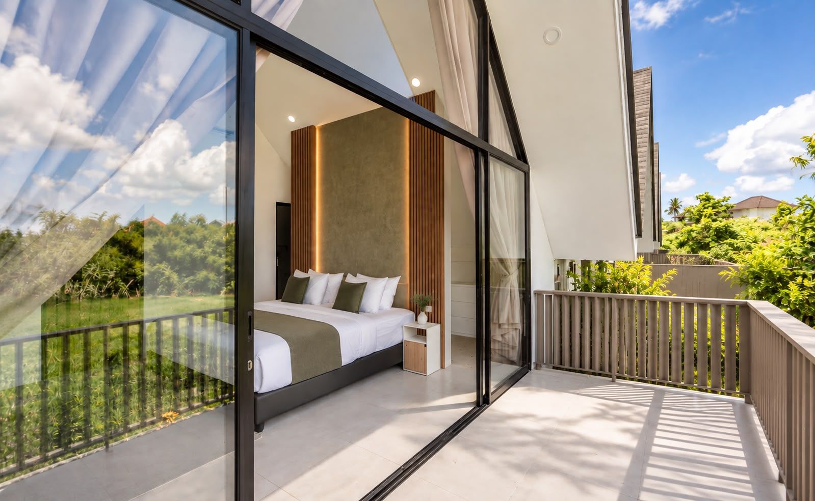 A modern bedroom with a large bed, a bedside table, and a view of greenery through floor-to-ceiling windows.