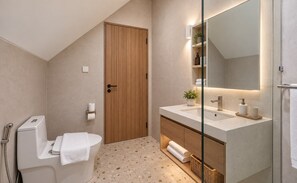 Un baño moderno con puerta de madera, inodoro blanco, lavabo con espejo y zona de ducha.