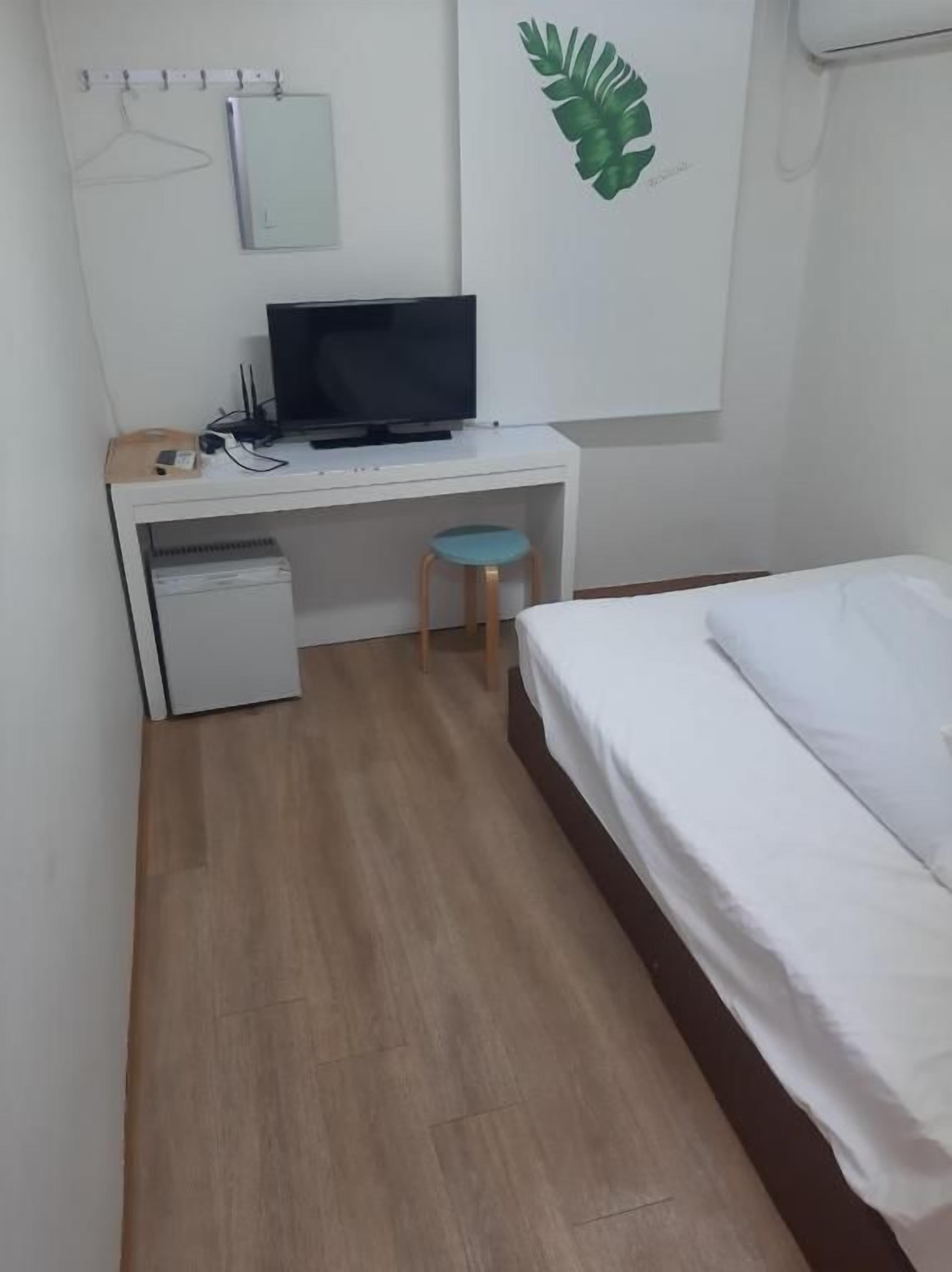 A bedroom with a bed, a desk with a computer, a chair, and a small cabinet.
