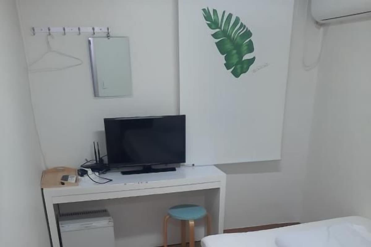 Un dormitorio con una cama, un escritorio con una computadora, una silla y un armario pequeño.