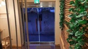Um saguão de hotel com balcão de recepção, elevador de vidro e parede decorada com plantas.