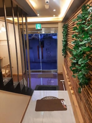 Eine Hotelhalle mit einer Rezeption, einem gläsernen Aufzug und einer mit Grünpflanzen gestalteten Wand.