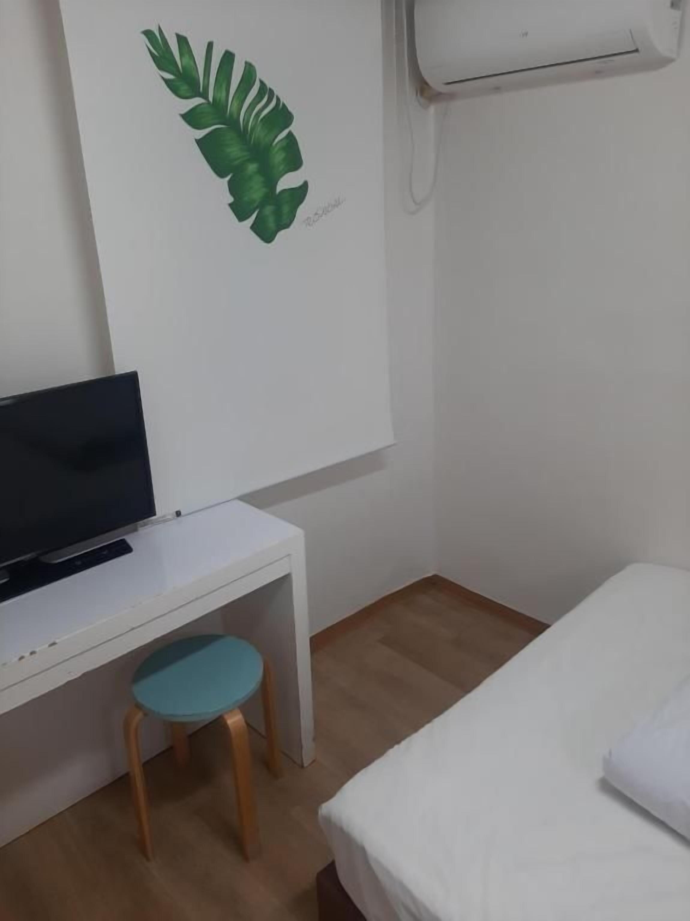 A room with a bed, a desk with a television, a small stool, and a wall-mounted air conditioner.