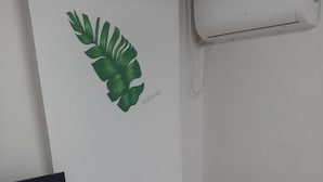 Een kamer met een bed, een bureau met een televisie, een klein krukje en een wandairconditioner.