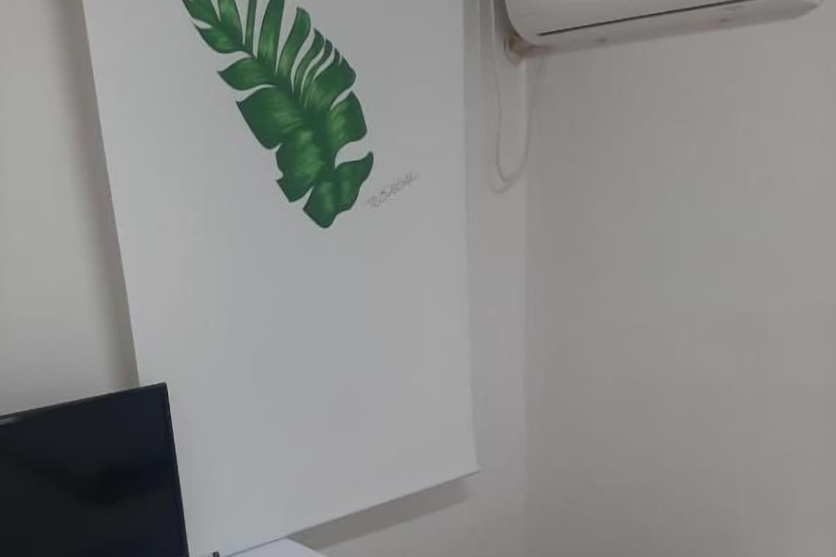 Ein Zimmer mit einem Bett, einem Schreibtisch mit Fernseher, einem kleinen Hocker und einer Wand-Klimaanlage.