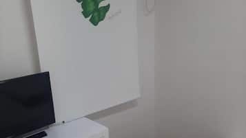A room with a bed, a desk with a television, a small stool, and a wall-mounted air conditioner.