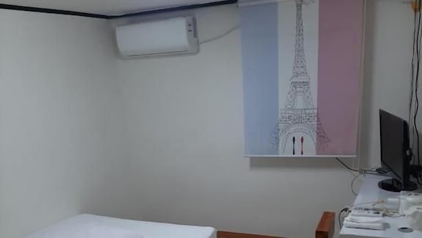 Een slaapkamer met een bed, een bureau, een stoel, een computer en een airconditioning.