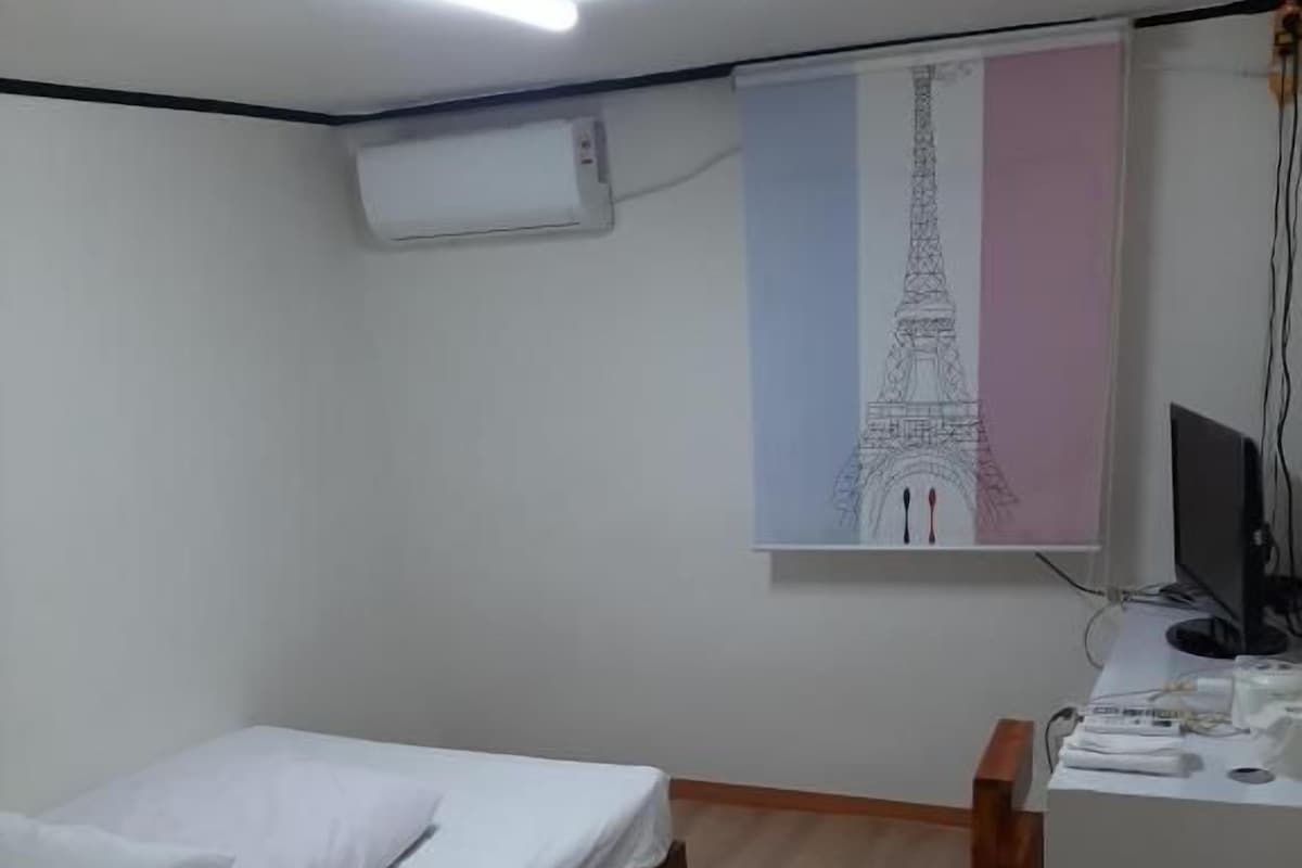 Een slaapkamer met een bed, een bureau, een stoel, een computer en een airconditioning.