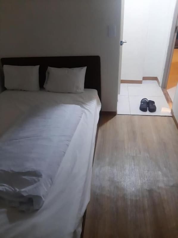 Una habitación de hotel con una cama, un par de zapatos en el suelo y una puerta que da a otra habitación.