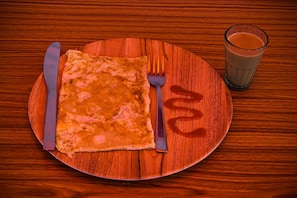 Ein Holztisch mit einem Teller, auf dem ein gefalteter Omelett, eine Gabel, ein Messer und ein Glas Orangensaft liegen.