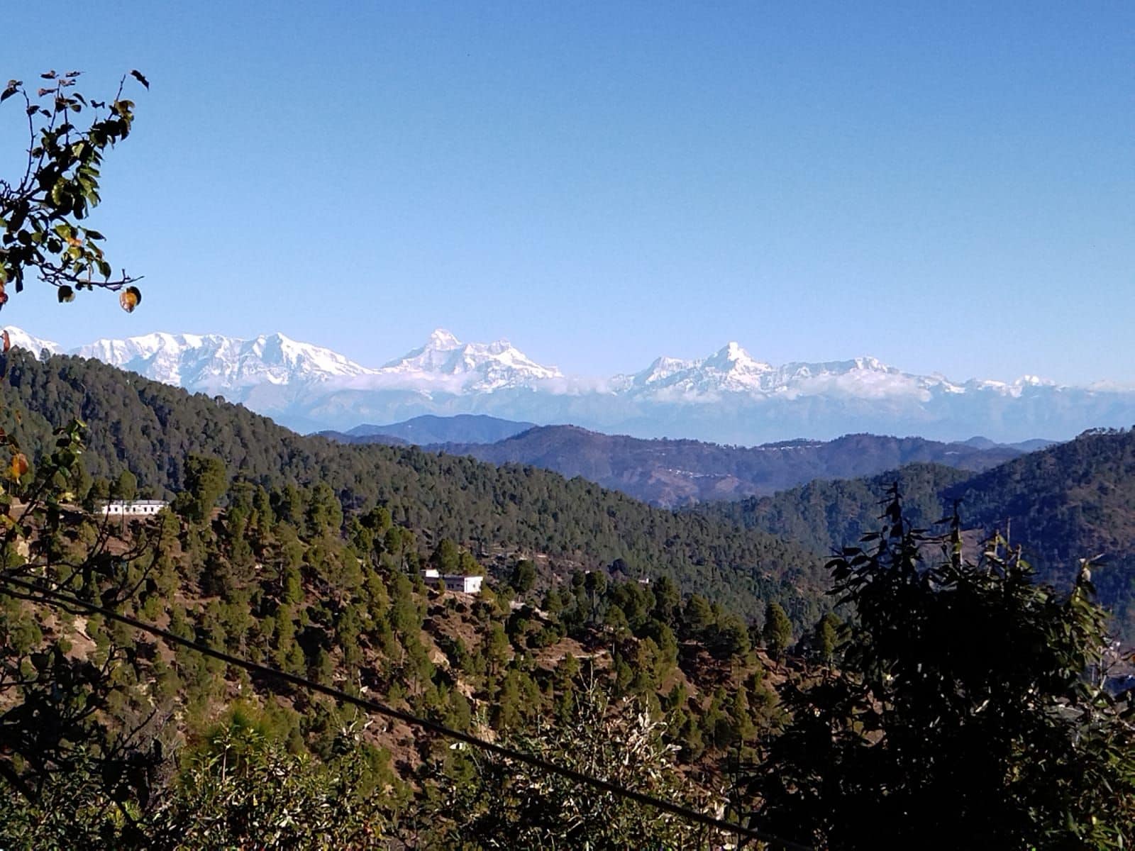 A mountainous landscape with a clear sky, a building in the foreground, and snow-capped peaks in the distance.