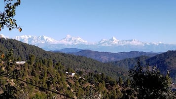 A mountainous landscape with a clear sky, a building in the foreground, and snow-capped peaks in the distance.