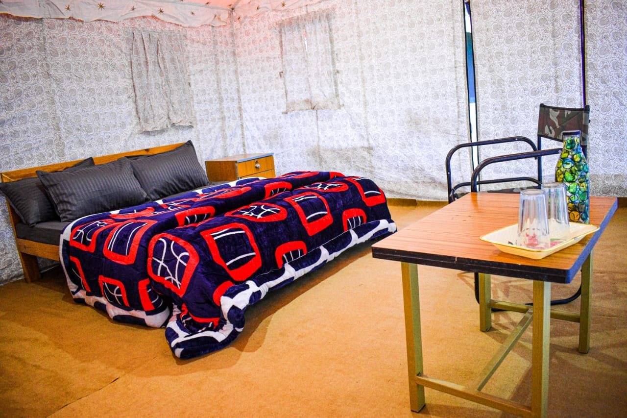 Una habitación con cama, una mesa y una silla. Tiene una pared con diseño y un ventanal con cortinas.