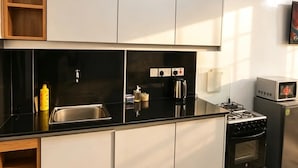 Een moderne keuken met een zwart aanrecht, een roestvrijstalen spoelbak en een ingebouwde oven. Links is een houten plankunit en rechts staat een magnetron.