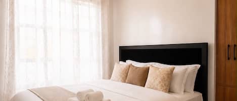 Una cama bien hecha con cabecera, una mesita de noche con toallas y una ventana con cortinas.