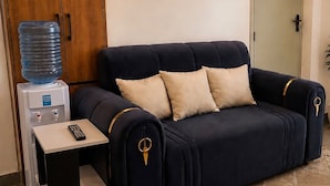 Een donkerblauwe bank met gouden accenten, een waterdispenser en een afstandsbediening op een tafeltje.