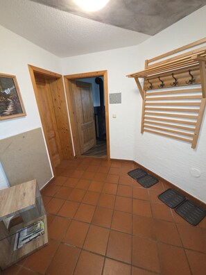 A hallway with a wooden door, a tiled floor, a wall-mounted rack with hooks, and a small shelf with items. - Cozy vacation rental on the Guldensteig trail in the heart of the Bavarian Forest National Park (Neuschönau)