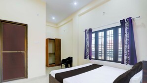 A bedroom with a bed, a wardrobe, a chair, and a window with curtains. - Collection O Varanasi Ashta Bhuji Temple (Varanasi)