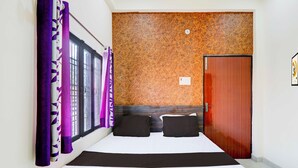 A hotel room with a bed, a wooden headboard, a door, and a window with purple curtains. - Collection O Varanasi Ashta Bhuji Temple (Varanasi)