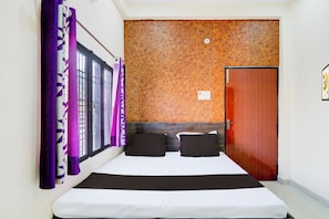 A hotel room with a bed, a wooden headboard, a door, and a window with purple curtains. - Collection O Varanasi Ashta Bhuji Temple (Varanasi)