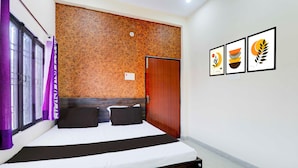 A hotel room with a bed, a wooden headboard, a door, and three framed pictures on the wall. - Collection O Varanasi Ashta Bhuji Temple (Varanasi)