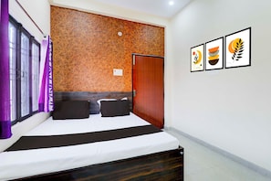 A hotel room with a bed, a wooden headboard, a door, and three framed pictures on the wall. - Collection O Varanasi Ashta Bhuji Temple (Varanasi)
