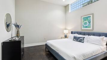 A modern bedroom with a large bed, a dresser, a mirror, and a painting on the wall.