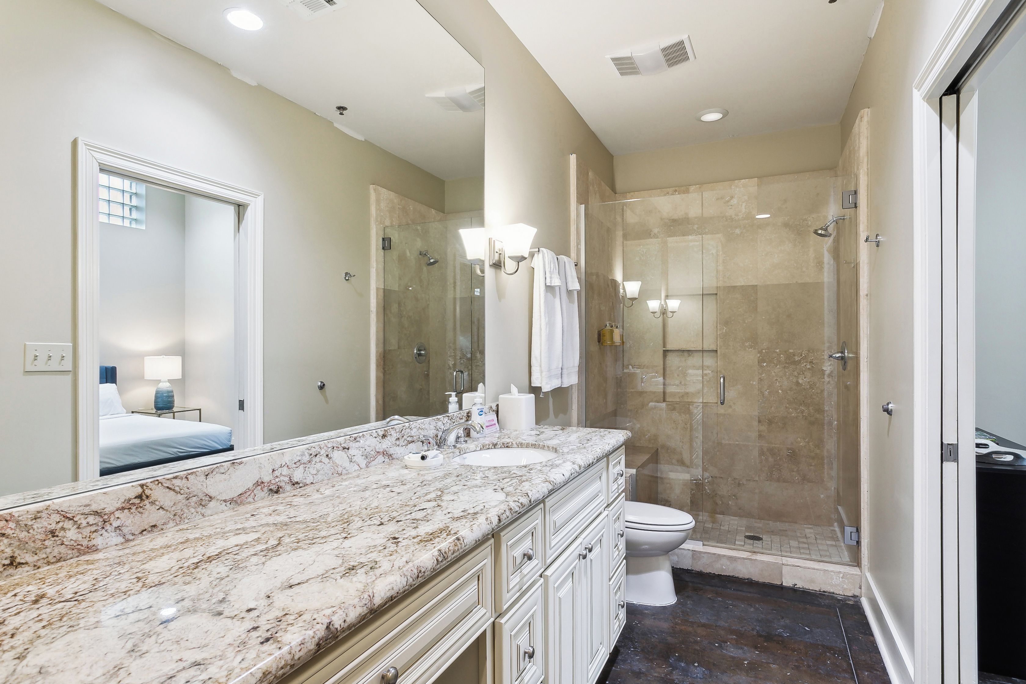 A bathroom with a marble countertop, a glass-enclosed shower, and a toilet.