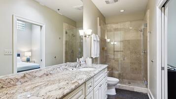 A bathroom with a marble countertop, a glass-enclosed shower, and a toilet.