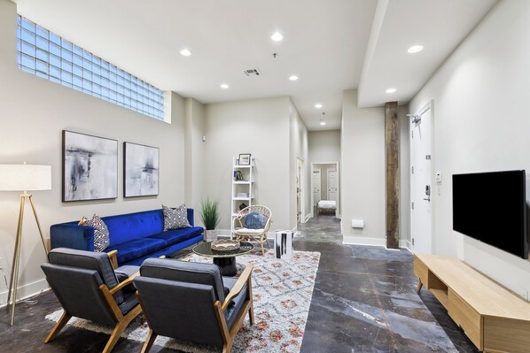A modern living room with a blue sofa, a coffee table, and a flat-screen TV. - Historic Bywater 2BR Near Frenchmen St (New Orleans)
