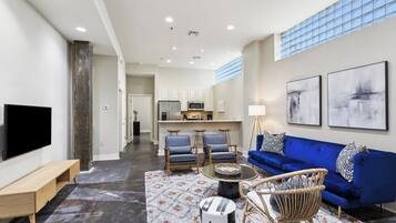 A modern living room with a blue sofa, two armchairs, a coffee table, and a flat-screen TV.