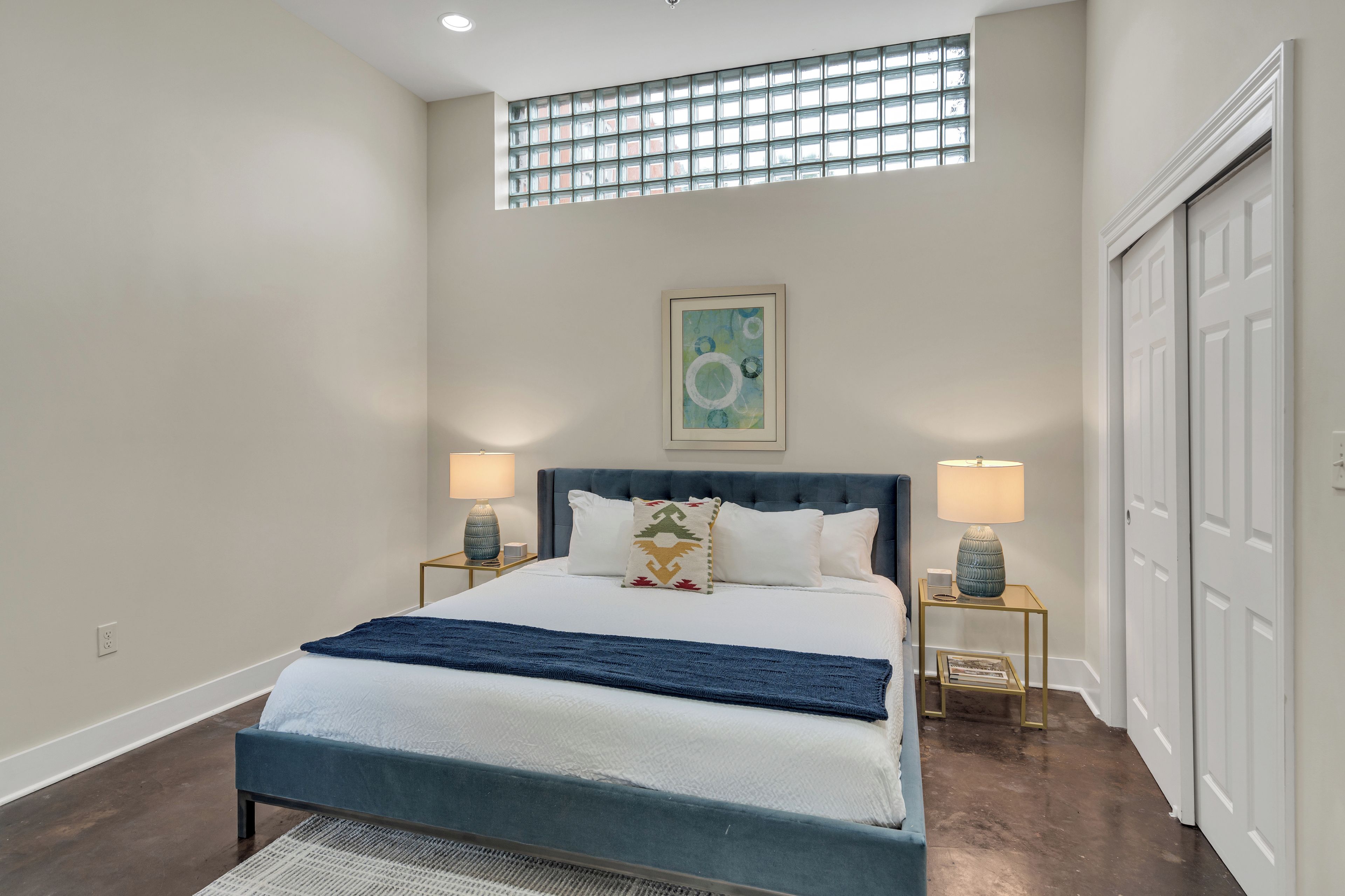 Quarto com cama, duas luminárias de cabeceira, janela e porta.