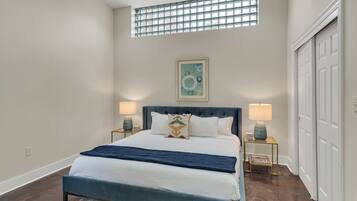 Quarto com cama, duas luminárias de cabeceira, janela e porta.