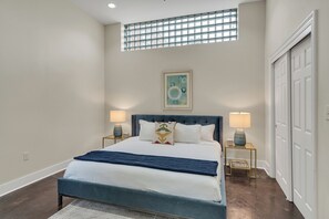 Quarto com cama, duas luminárias de cabeceira, janela e porta.