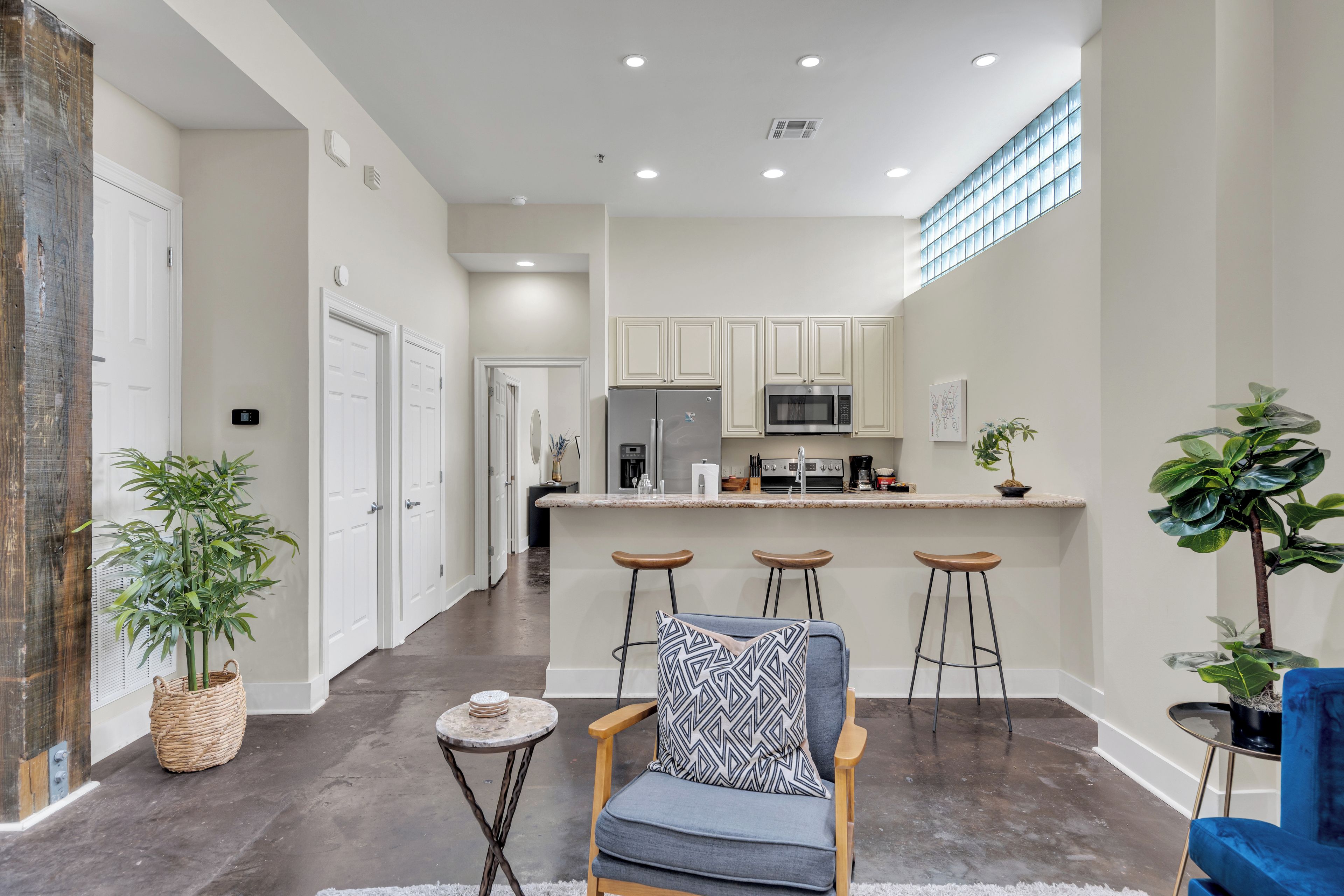 A modern kitchen with a central island, bar stools, and a seating area with a patterned cushion.