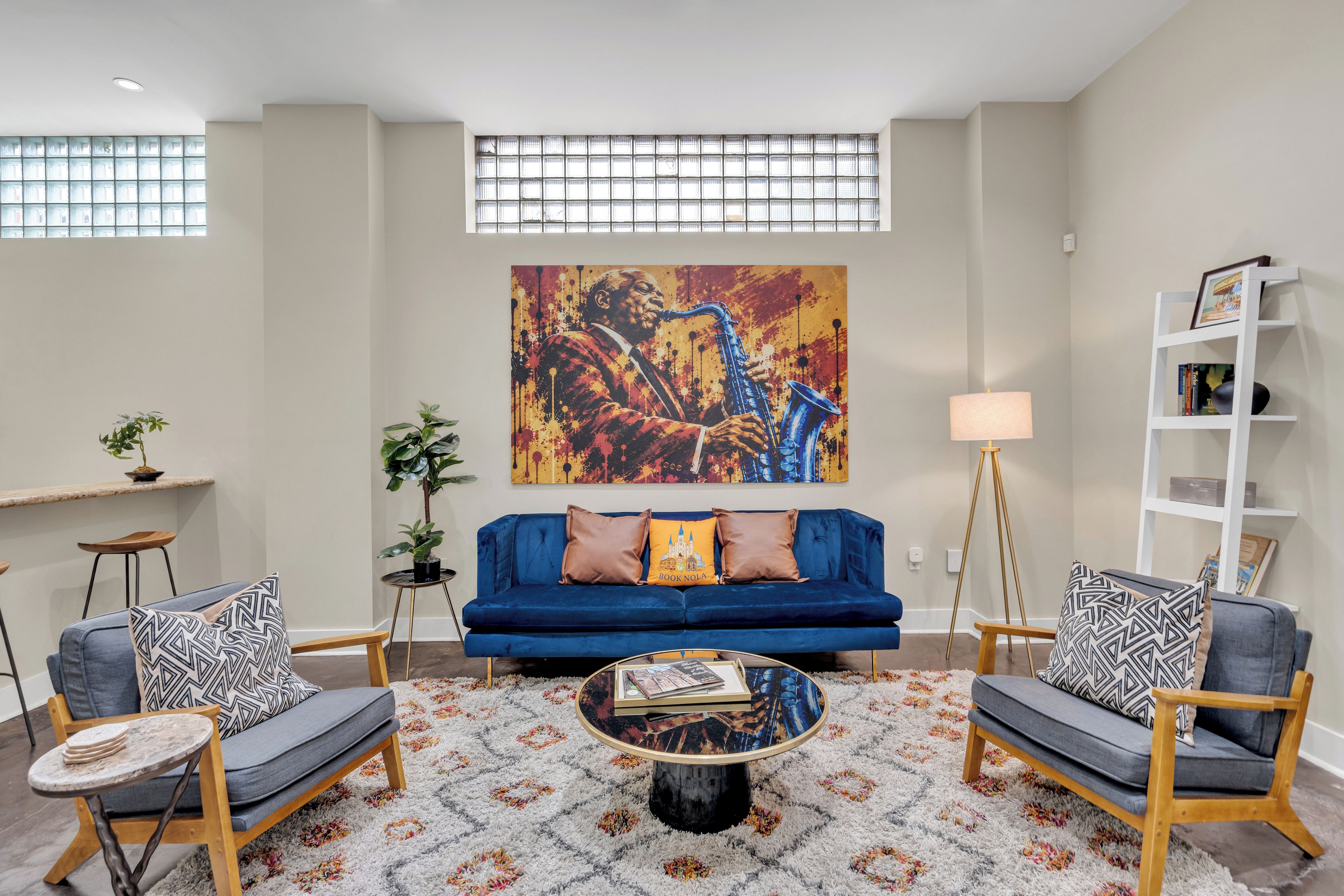 Ein Wohnzimmer mit einem blauen Sofa, zwei Sesseln, einem Couchtisch und einem großen abstrakten Gemälde an der Wand.