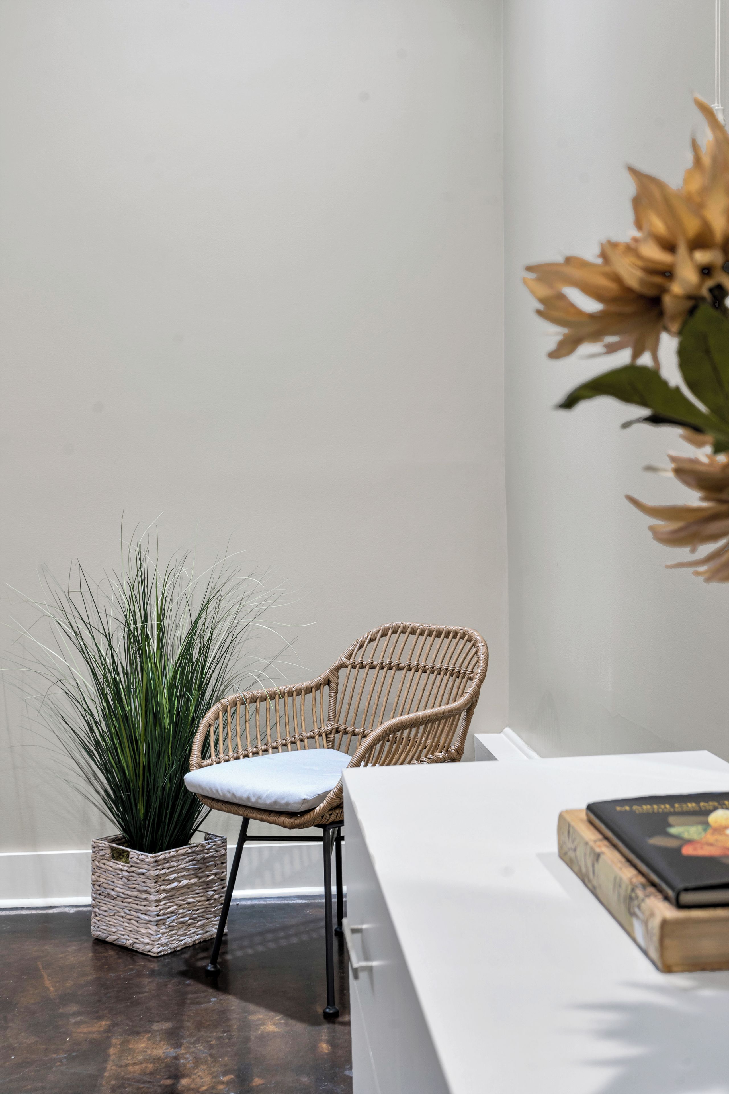 A wicker chair with a cushion, a woven basket with a plant, and a book on a table.