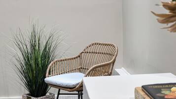 A wicker chair with a cushion, a woven basket with a plant, and a book on a table.