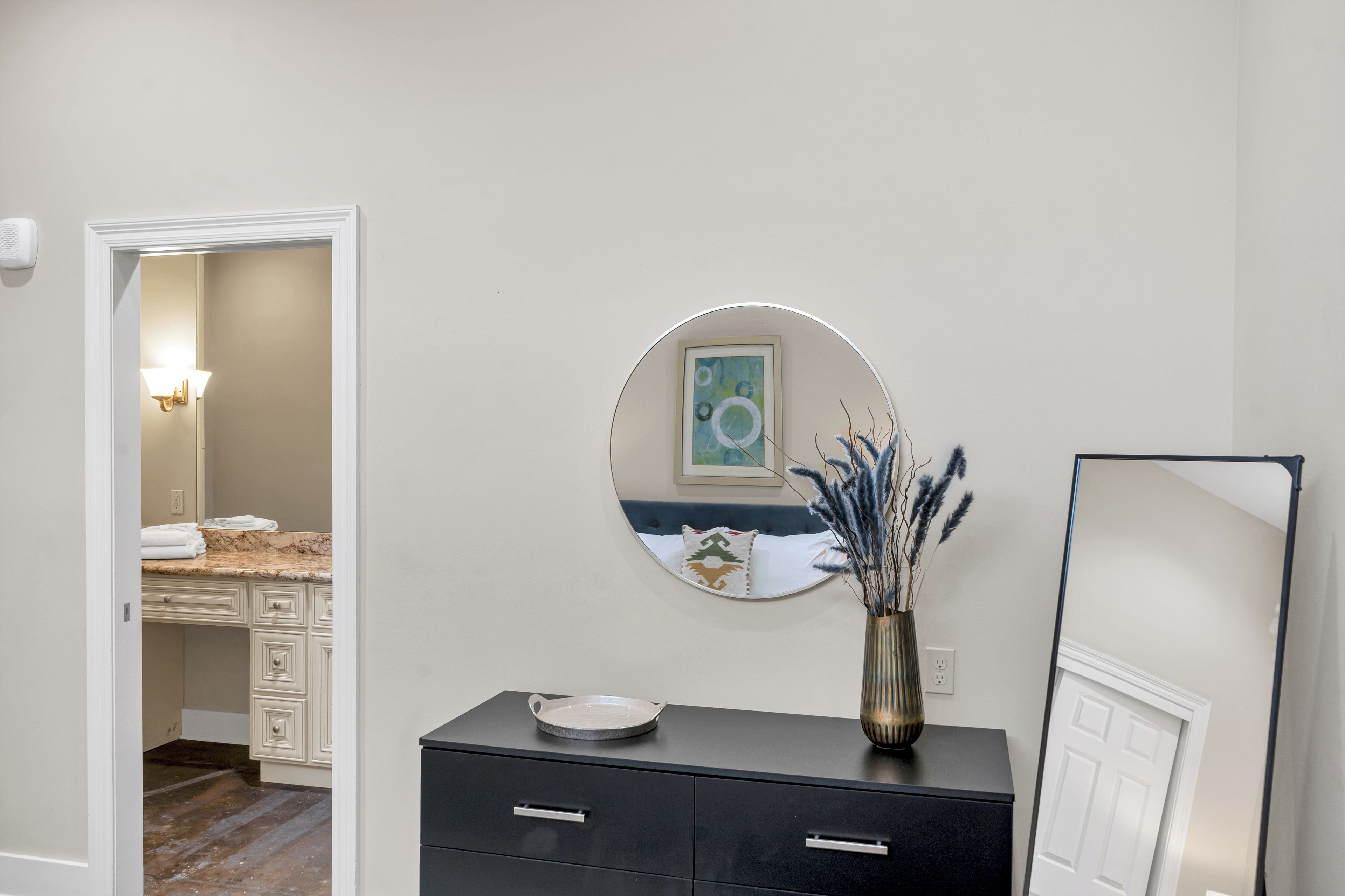 A modern bathroom with a vanity, a round mirror, and a decorative vase.