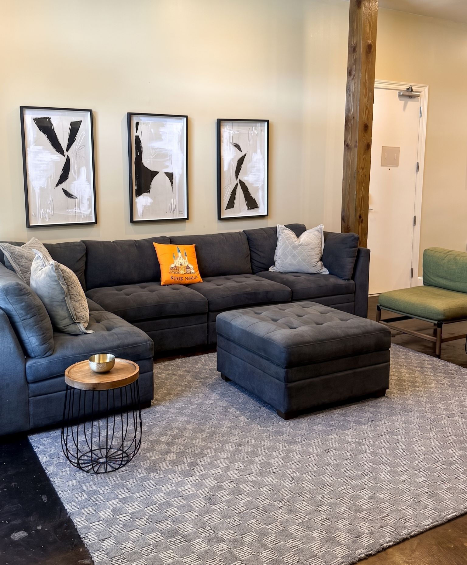A modern living room with a sectional sofa, a coffee table, and a patterned rug. There are three framed abstract paintings on the wall.