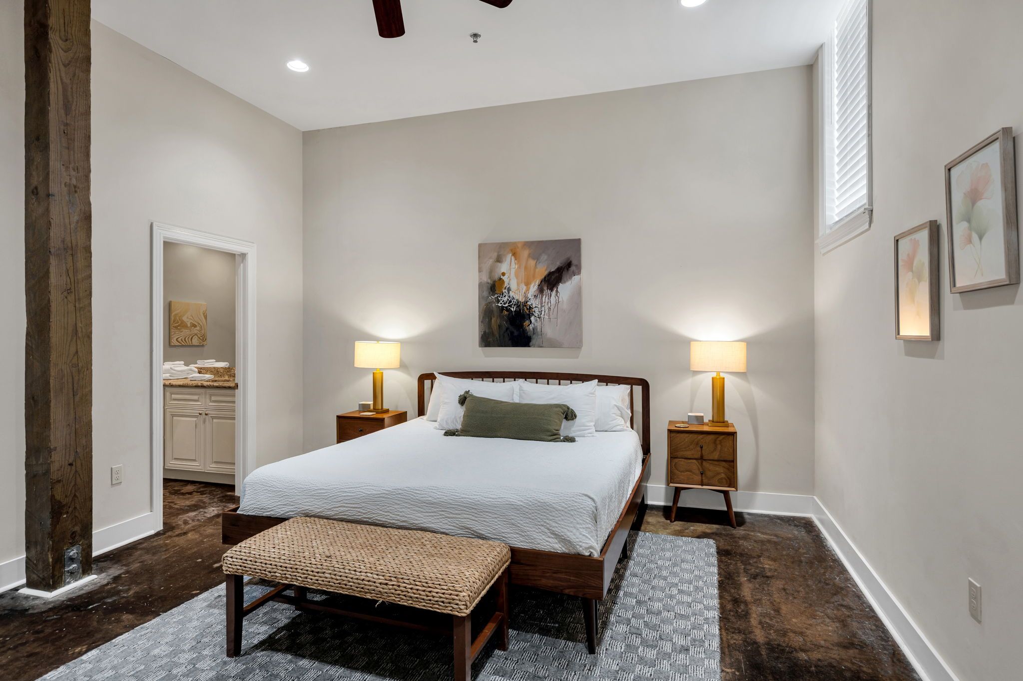 A bedroom with a large bed, two bedside tables with lamps, a bench, and artwork on the walls.