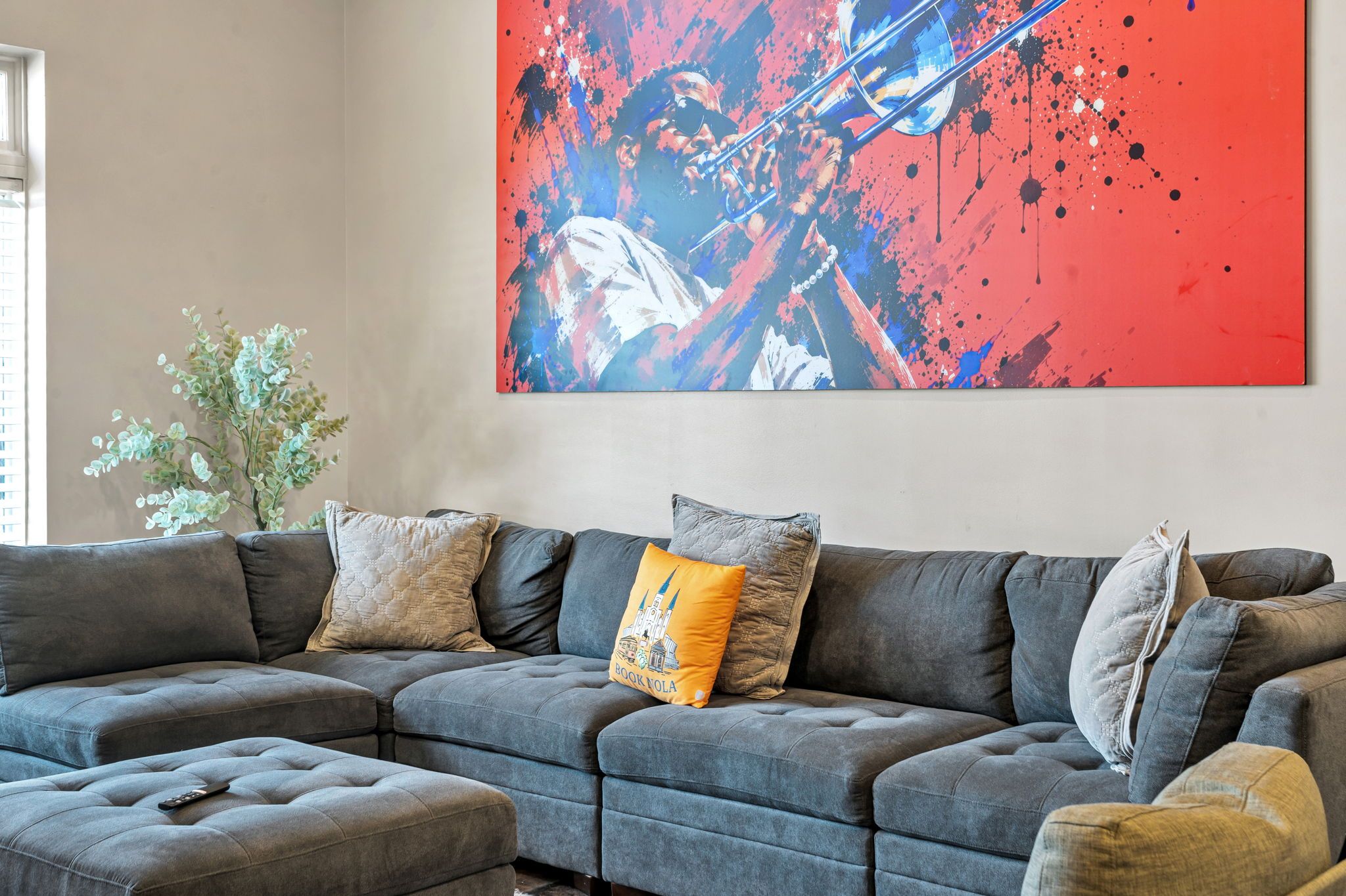 A modern living room with a sectional sofa, a potted plant, and a large abstract painting.